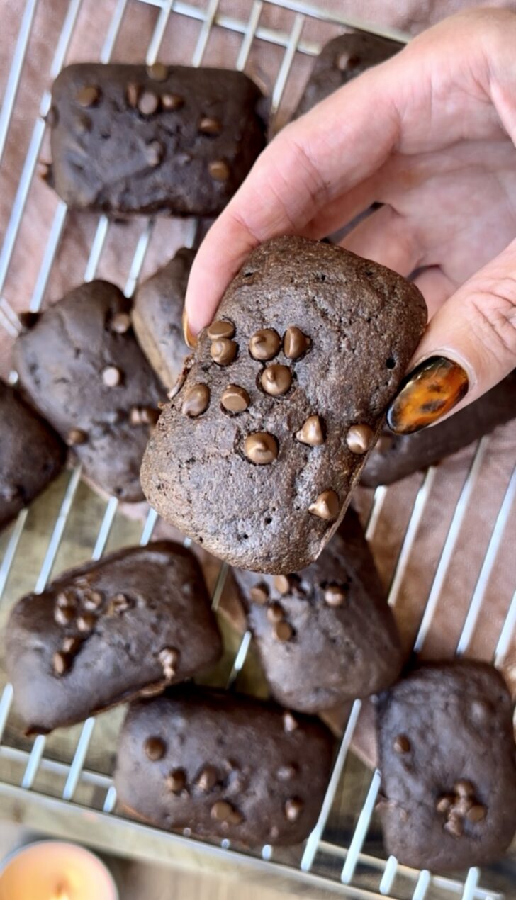 Close-up of a hand holding a soft, fudgy mini chocolate pumpkin cake topped with melted chocolate chips.