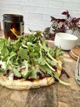 High-protein pita pizza topped with arugula, melted cheese, lentils, and balsamic glaze on a wooden cutting board