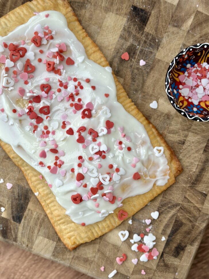 A homemade giant raspberry pop tart made with Greek yogurt dough and raspberry chia seed jam, topped with a creamy frosting and festive sprinkles.