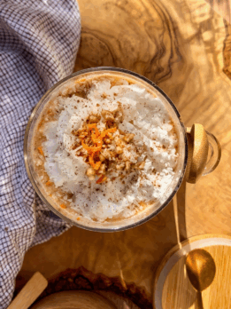 High-protein coconut carrot cake overnight oats in a glass jar topped with shredded coconut, grated carrots, and cinnamon on a wooden table with natural light