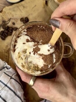 High-protein tiramisu overnight oats topped with creamy tofu and cottage cheese layer and cocoa powder, served in a glass mug with espresso and oats for a healthy performance-nutrition breakfast.