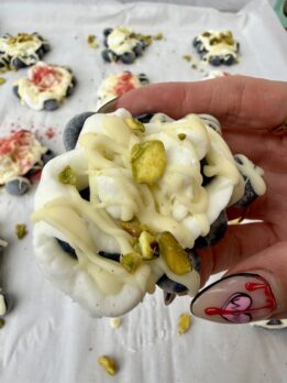 High-protein frozen blueberry yogurt cluster topped with white chocolate drizzle and chopped pistachios on parchment paper