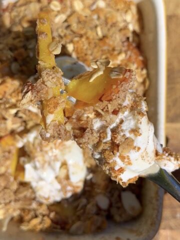 High-protein peach cobbler with oats and Greek yogurt, close-up of a spoonful showing juicy baked peaches, crumb topping, and creamy yogurt drizzle