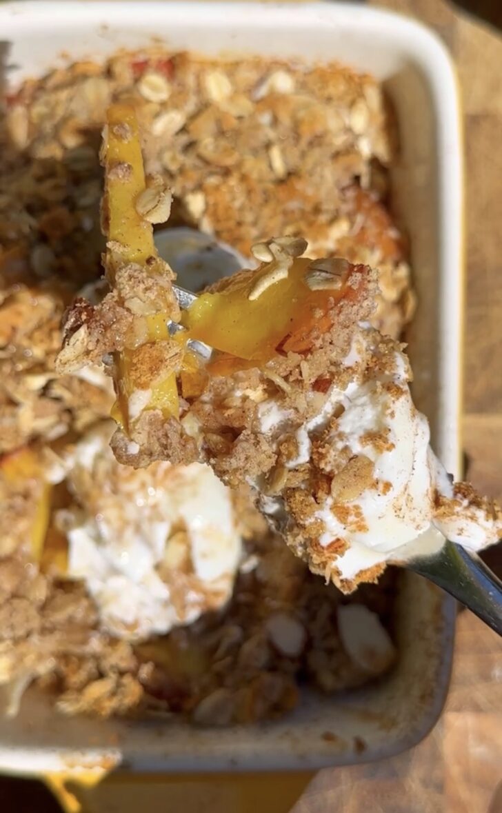High-protein peach cobbler with oats and Greek yogurt, close-up of a spoonful showing juicy baked peaches, crumb topping, and creamy yogurt drizzle