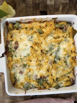 Creamy high-protein pasta bake made with rotini pasta, melted cheese, spinach, and sun-dried tomatoes baked until golden and bubbly in a white casserole dish. Cozy protein-packed dinner recipe perfect for meal prep, weeknight dinners, or healthy comfort food.