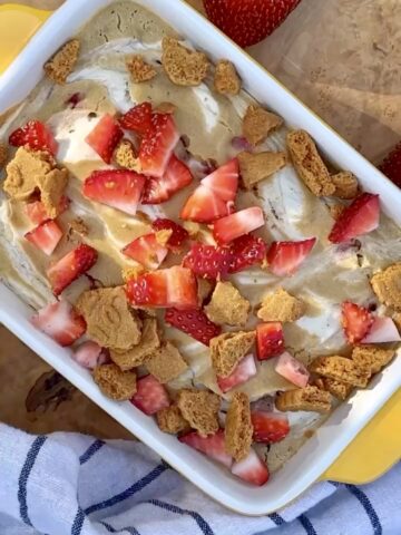 Strawberry cheesecake baked oats in a baking dish, topped with fresh strawberries and creamy cheesecake swirl, soft and golden with a high-protein texture.