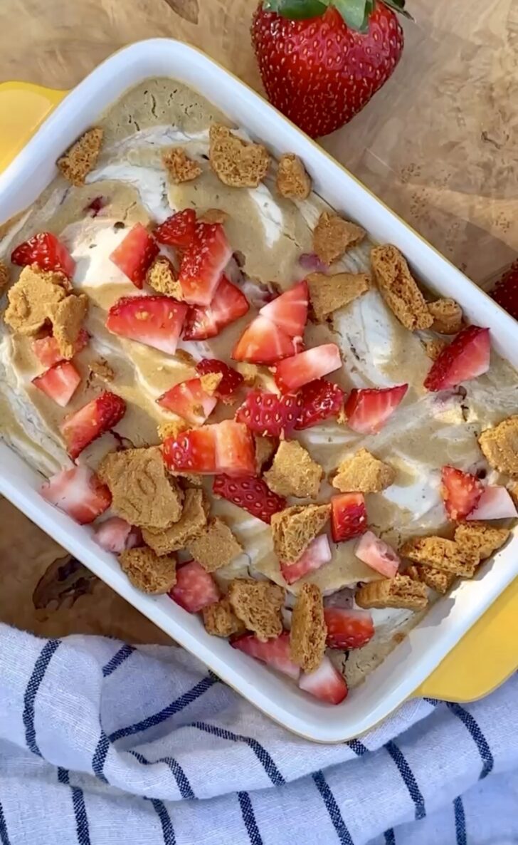 Strawberry cheesecake baked oats in a baking dish, topped with fresh strawberries and creamy cheesecake swirl, soft and golden with a high-protein texture.