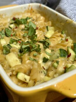 Creamy no-boil baked pasta with zucchini, pesto cream sauce, melted cheese, and fresh basil baked in a yellow casserole dish.