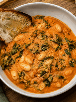 Creamy roasted tomato and cannellini bean stew with kale, served with toasted crusty bread in a ceramic bowl.
