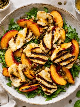 Overhead photo of a grilled peach halloumi salad with arugula, avocado, pumpkin seeds, basil, and homemade lemon Dijon dressing.