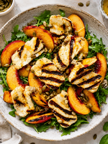 Overhead photo of a grilled peach halloumi salad with arugula, avocado, pumpkin seeds, basil, and homemade lemon Dijon dressing.