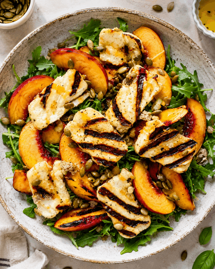 Overhead photo of a grilled peach halloumi salad with arugula, avocado, pumpkin seeds, basil, and homemade lemon Dijon dressing.
